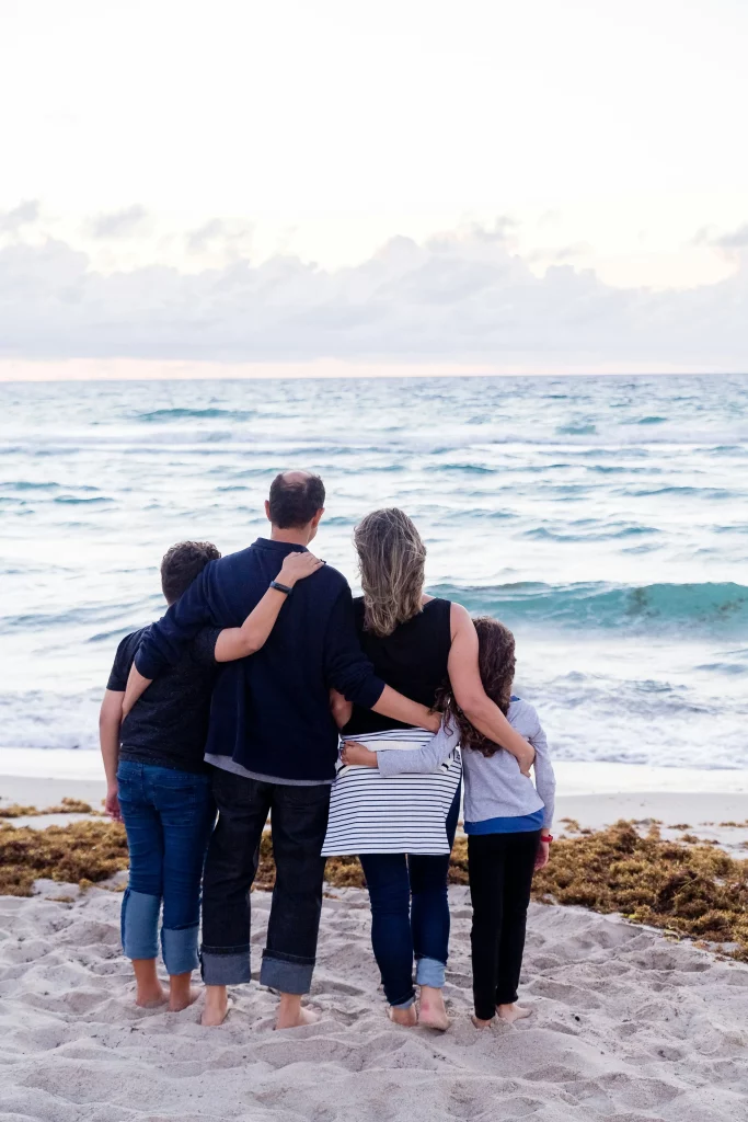 Famille unie de dos observant l'océan depuis une plage de sable fin.
